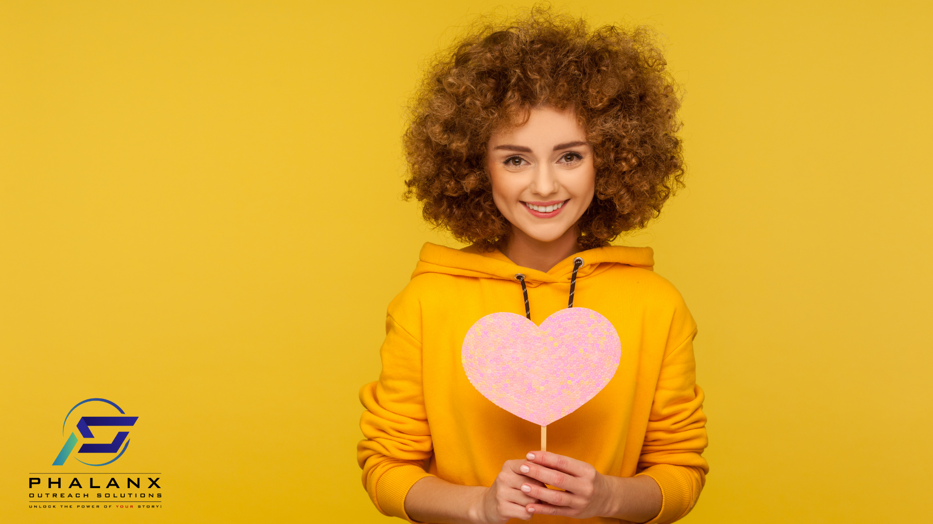 A young woman in a yellow hoodie smiles while holding a pink, heart-shaped cutout, standing against a bright yellow background, with the Phalanx Outreach Solutions logo and tagline, "Unlock the Power of Your Story!" displayed in the bottom left corner.